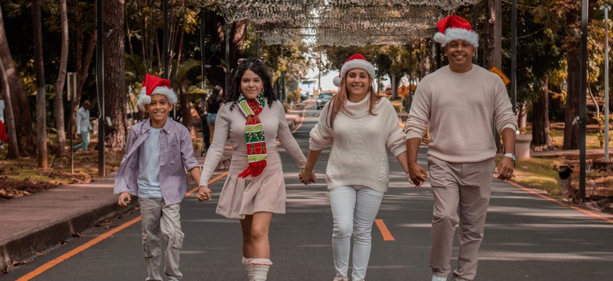 A joyful family walks down a decorated street wearing Christmas hats, symbolizing holiday spirit.