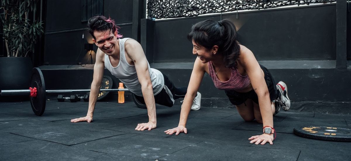 Man and woman doing pushups while smiling during a workout inside a Mexico City gym.